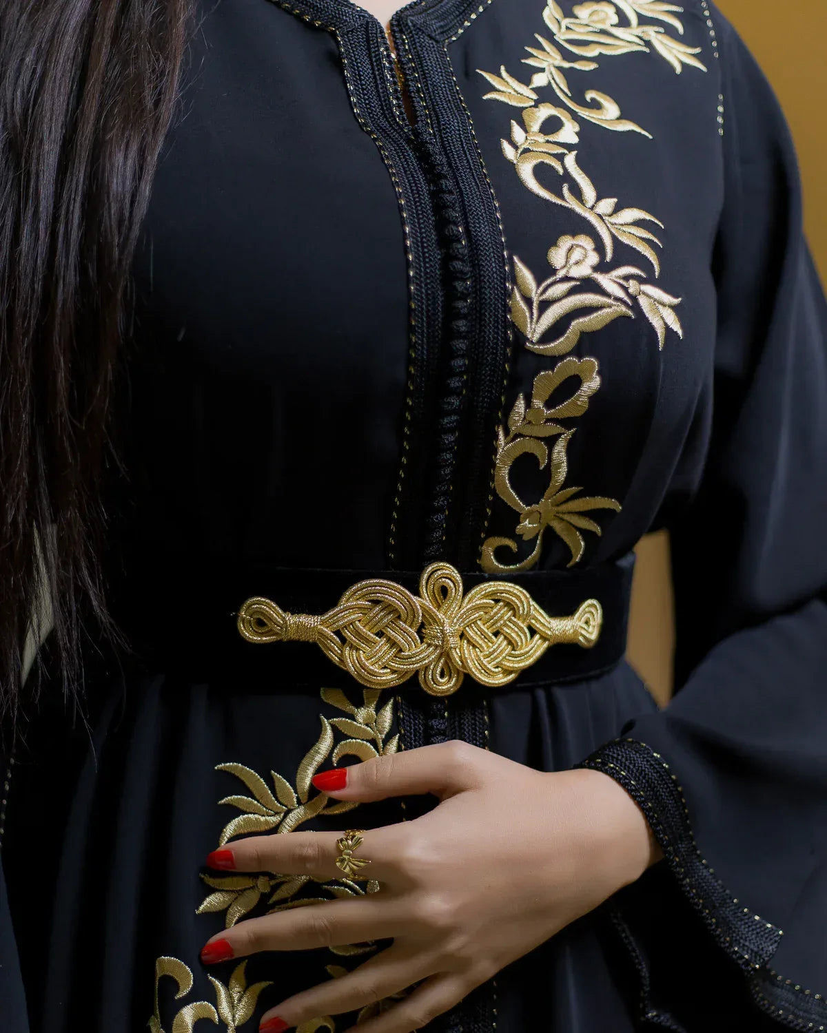 Detailed view of the decorative gold waist belt and hand placement on black caftan