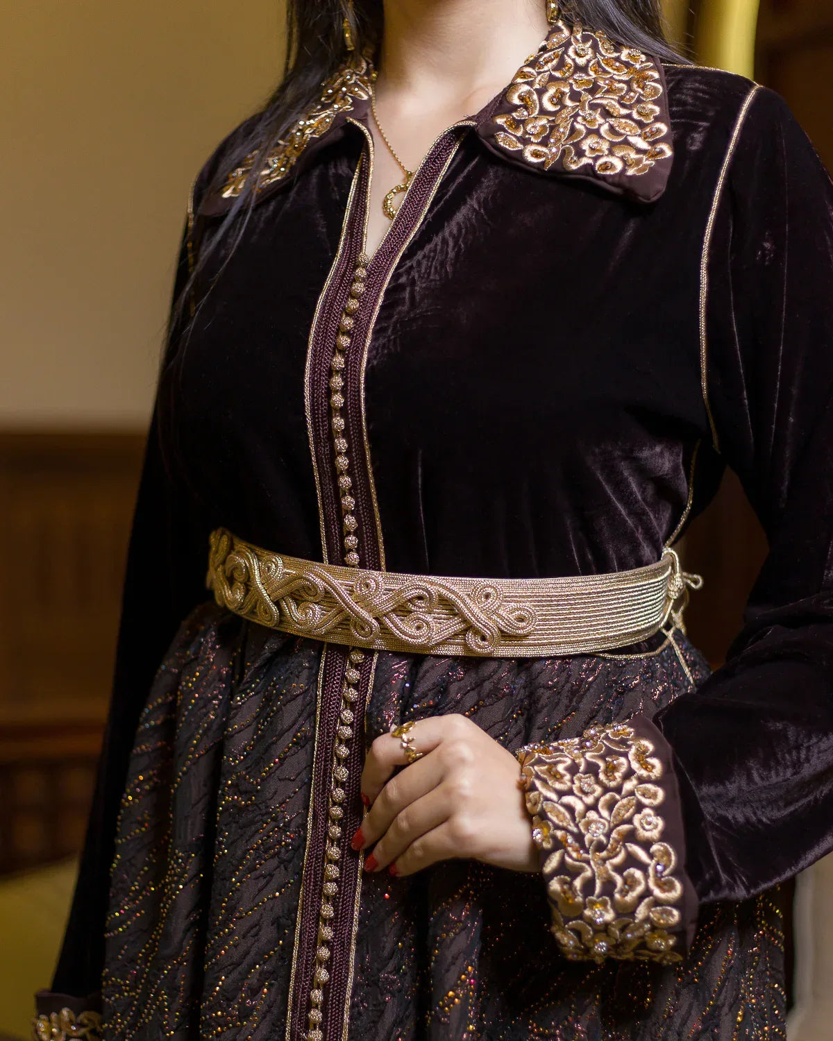 Close shot of the golden waist belt and central embroidery on the brown velvet dress.