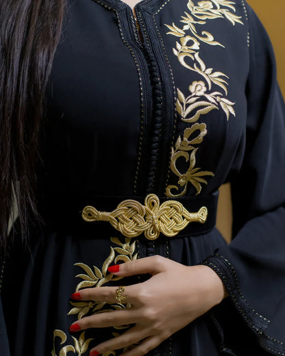 Detailed view of the decorative gold waist belt and hand placement on black caftan