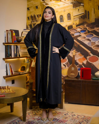 A woman in a black abaya NAGAM, standing in a room with a colorful rug and musical instruments.