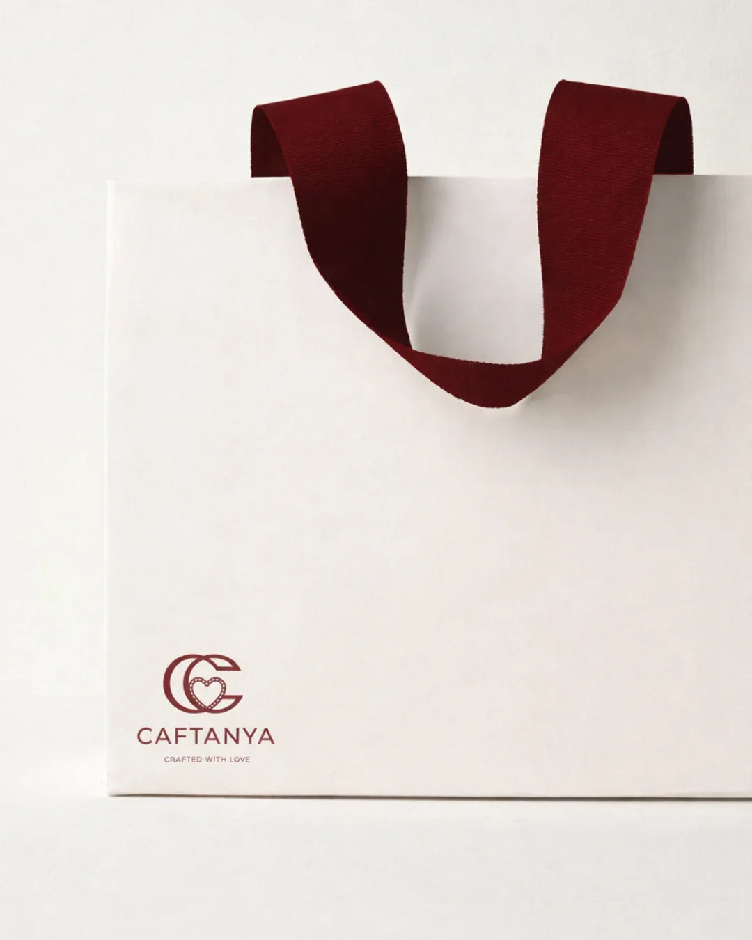 White paper bag with red handle and 'Caftanya' logo on a white background